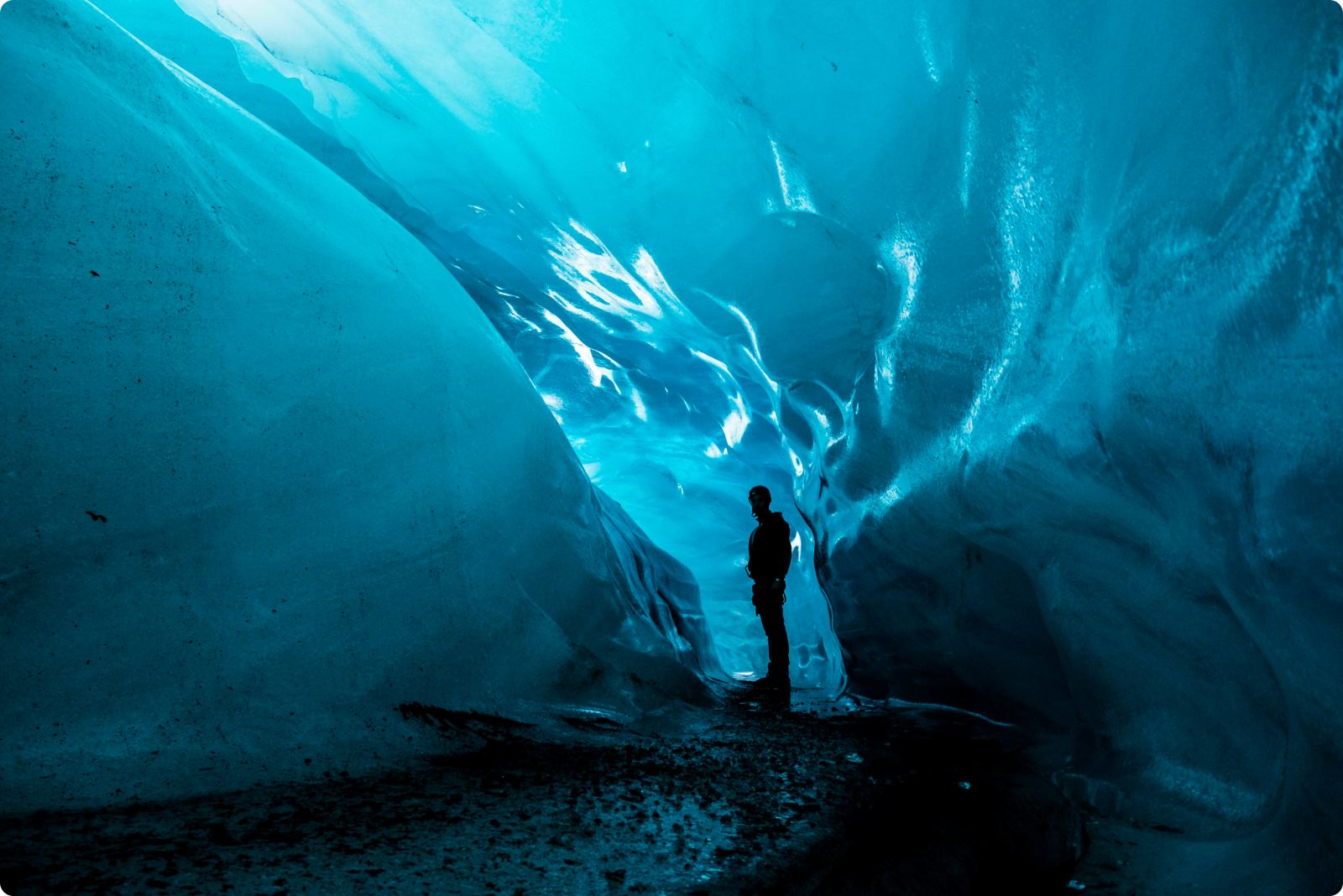 A person stands for scale inside a blue ice cave in Vatnajökull National Park.